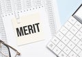 a yellow piece of paper with the text merit and the calculator are lying on the notepad Royalty Free Stock Photo