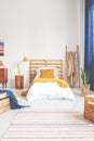 Yellow pillow and blanket on comfortable white wooden bed in teenager bedroom with stripped carpet on the floor