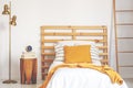 Yellow pillow and blanket on white wooden single bed in natural bedroom, real photo