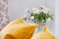 Yellow pillows on couch in living room, focus on beautiful flowers in vase white ranunculus near wall cute decoration at home