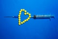 yellow pills are laid out in the shape of a heart and like an arrow pierced by a syringe