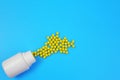 Yellow pills spilled out from white bottle on blue background, copy space Royalty Free Stock Photo