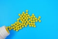 Yellow pills spilled out from white bottle on blue background Royalty Free Stock Photo