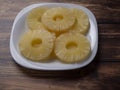 Yellow pineapple rings on a white plate on a wooden table close up. Royalty Free Stock Photo