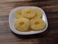 Yellow pineapple rings on a white plate on a wooden table close up. Royalty Free Stock Photo