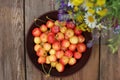 Yellow and pink cherries in a bowl, and midsummer wild flowers on a vintage wooden board background.