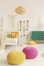 Yellow and pink pouf in the middle of boho female bedroom with green cabinet, flower board, single bed and macrame on the wall