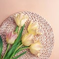 Yellow-pink tulip flowers on wicker place mat on peachy background. Spring holiday concept. Top view, flat lay Royalty Free Stock Photo