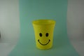 A yellow plastic cup with a smiling face, so it is very popular with children. Blue Background. Kids toys, kid friendly