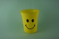 A yellow plastic cup with a smiling face, so it is very popular with children. Blue Background. Kids toys, kid friendly