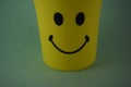 A yellow plastic cup with a smiling face, so it is very popular with children. Blue Background. Kids toys, kid friendly