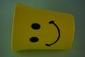 A yellow plastic cup with a smiling face, so it is very popular with children. Blue Background. Kids toys, kid friendly