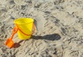 Yellow plastic sand pail with orange shovel at a sandy beach