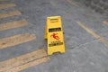 Yellow plastic sign with red symbol of slip and black text of caution wet floor on the floor.