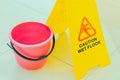 A yellow plastic warning sign that says caution wet floor and a pink bucket stand on a light floor