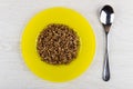 Yellow plate with boiled buckwheat, spoon on wooden table