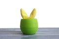 Yellow plush ears of a hare stick out of a green plastic pot on a wooden background.