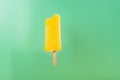 Yellow popsicle with a bite on light green background