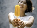 Yellow popsicle in happy smiling beautiful Asian woman`s hand. Royalty Free Stock Photo