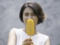 Yellow popsicle in happy smiling beautiful Asian woman`s hand. Royalty Free Stock Photo