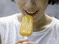 Yellow popsicle in happy smiling beautiful Asian woman`s hand. Royalty Free Stock Photo