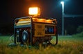 Yellow portable generator with bright work light active at night on grassy field. Diesel engine, electrical power supply for Royalty Free Stock Photo