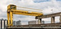 A yellow portal crane with a silo complex in the background