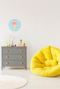 Yellow pouf next to a grey chest of drawers and ice-cream poster