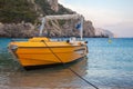 A yellow private boat in the beach. The speed water vehicle docking in the shoreline. A mountainous rock formation secluding the a Royalty Free Stock Photo
