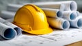 Yellow protective construction helmet placed on detailed architectural blueprints with rolled-up project plans surrounding it on a Royalty Free Stock Photo