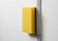 A yellow rectangular sponge with porous texture is adhered to a white wall. It has a green scrubbing Royalty Free Stock Photo