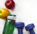 Yellow and red apples, a green water bottle and two blue dumbbells on a white background. Royalty Free Stock Photo