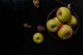 Yellow and red apples in wooden bowl standing on black wooden table background with some red dry autumn leaves around Royalty Free Stock Photo