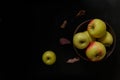 Yellow and red apples in wooden bowl standing on black wooden table background with some red dry autumn leaves around Royalty Free Stock Photo