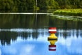 Yellow red buoy on a calm river to mark the shipping route in the upper reaches of a weir, reed belt in the background
