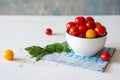 Yellow and red cherry tomatoes in a white bowl on a blue napkin. A bunch of green. Royalty Free Stock Photo