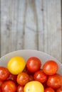 Yellow and red cherry tomatoes in a white bowl on a wooden table. Photo with copy space Royalty Free Stock Photo