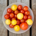 Yellow and red cherry tomatoes in a white bowl on a wooden table. Top view Royalty Free Stock Photo