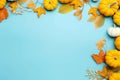 Yellow and red dried leaves and small orange pumpkins on blue background, top view, copy space. Halloween, Thanksgiving holiday