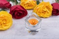 Yellow and red roses and candle on white wooden background
