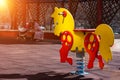 Yellow with red swing spring horse toy for kids on a children`s playground. Mother with baby in stroller at the background Royalty Free Stock Photo