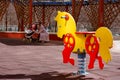 Yellow with red swing spring horse toy for kids on a children`s playground. Mother with baby in stroller at the background looks Royalty Free Stock Photo