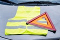 yellow reflective vest and warning triangle lie on hood of car. Safety on road in case of breakdown Royalty Free Stock Photo
