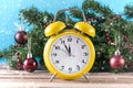 Yellow retro clock on wooden desk and fir Christmas tree with red ball decoration Royalty Free Stock Photo