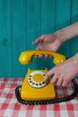 yellow retro telephone with a white disk and black numbers and a hand with a receiver on a turquoise wooden Royalty Free Stock Photo