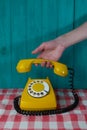 yellow retro telephone with a white disk and black numbers and a hand with a receiver on a turquoise wooden Royalty Free Stock Photo