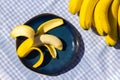 Yellow ripe bananas and one half peeled banana on the plate. Fresh organic fruits on blue tablecloth background on sunny day.