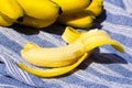Yellow ripe bananas and one half peeled banana with sharp shadows on blue tablecloth background. Fresh organic fruits on sunny day Royalty Free Stock Photo