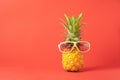 Yellow ripe pineapple in dark sunglasses on a red background. Funny face from a tropical fruit. Concept Copy space.