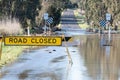 Yellow Road Closed sign to stop traffic driving over flooded bridge with muddy debris ridden water rushing in the background